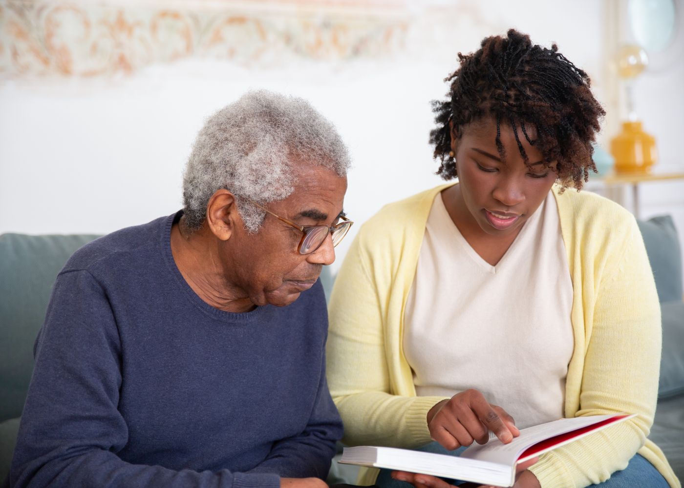 Older man and another adult sharing a book and conversation at home