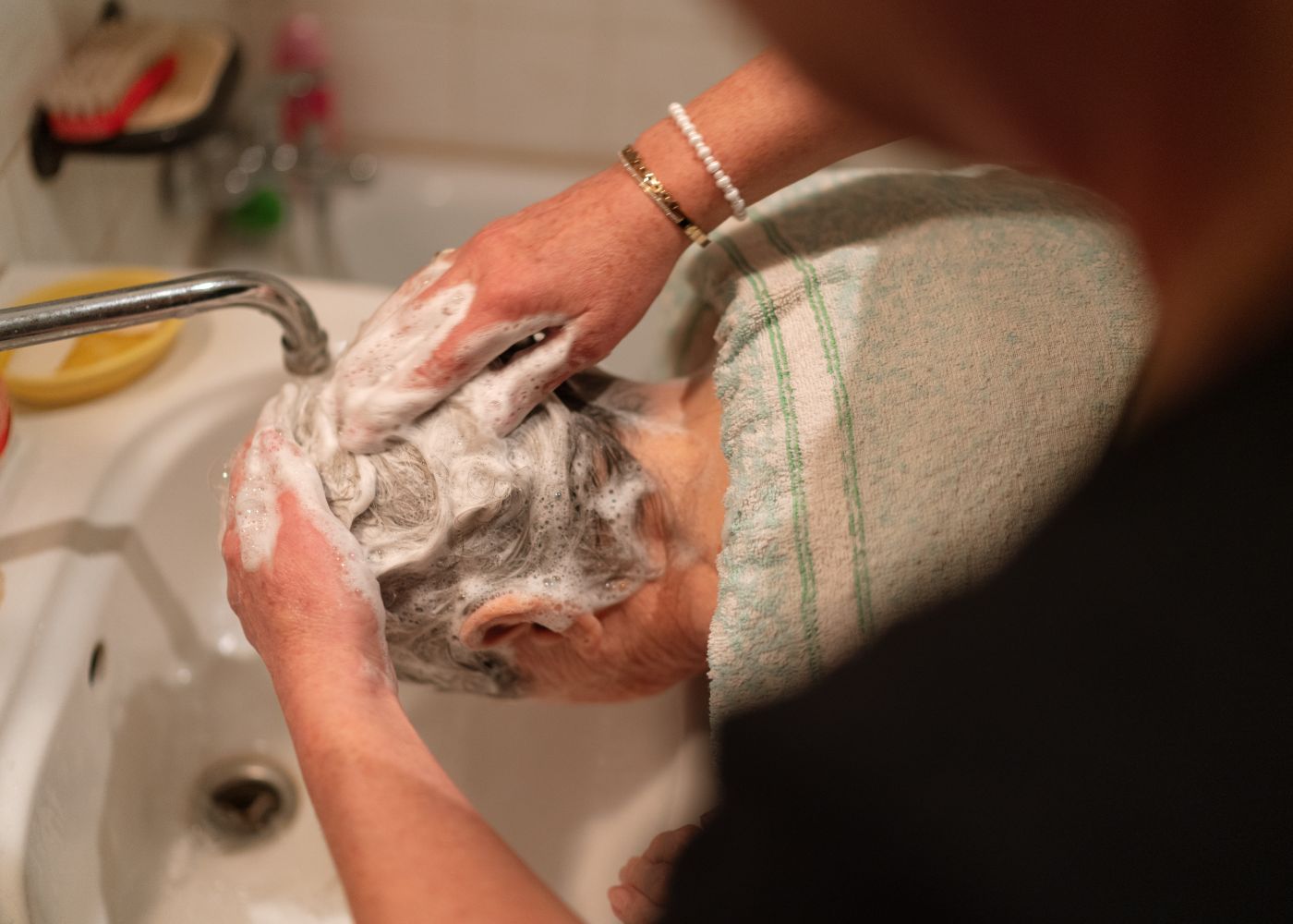 One person helping an older adult with hair grooming at home