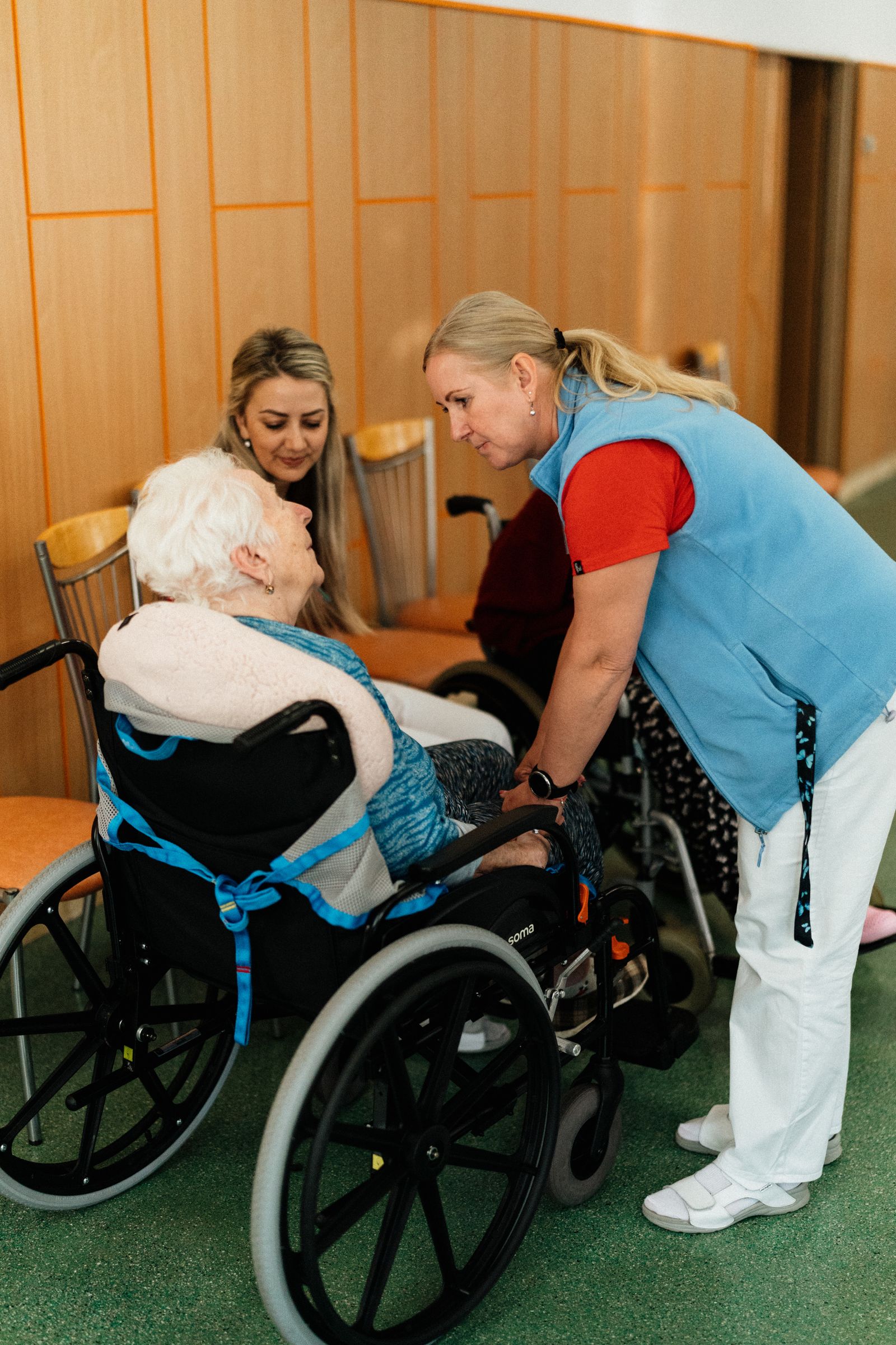 A caregiver speaking with an older woman seated in a wheelchair