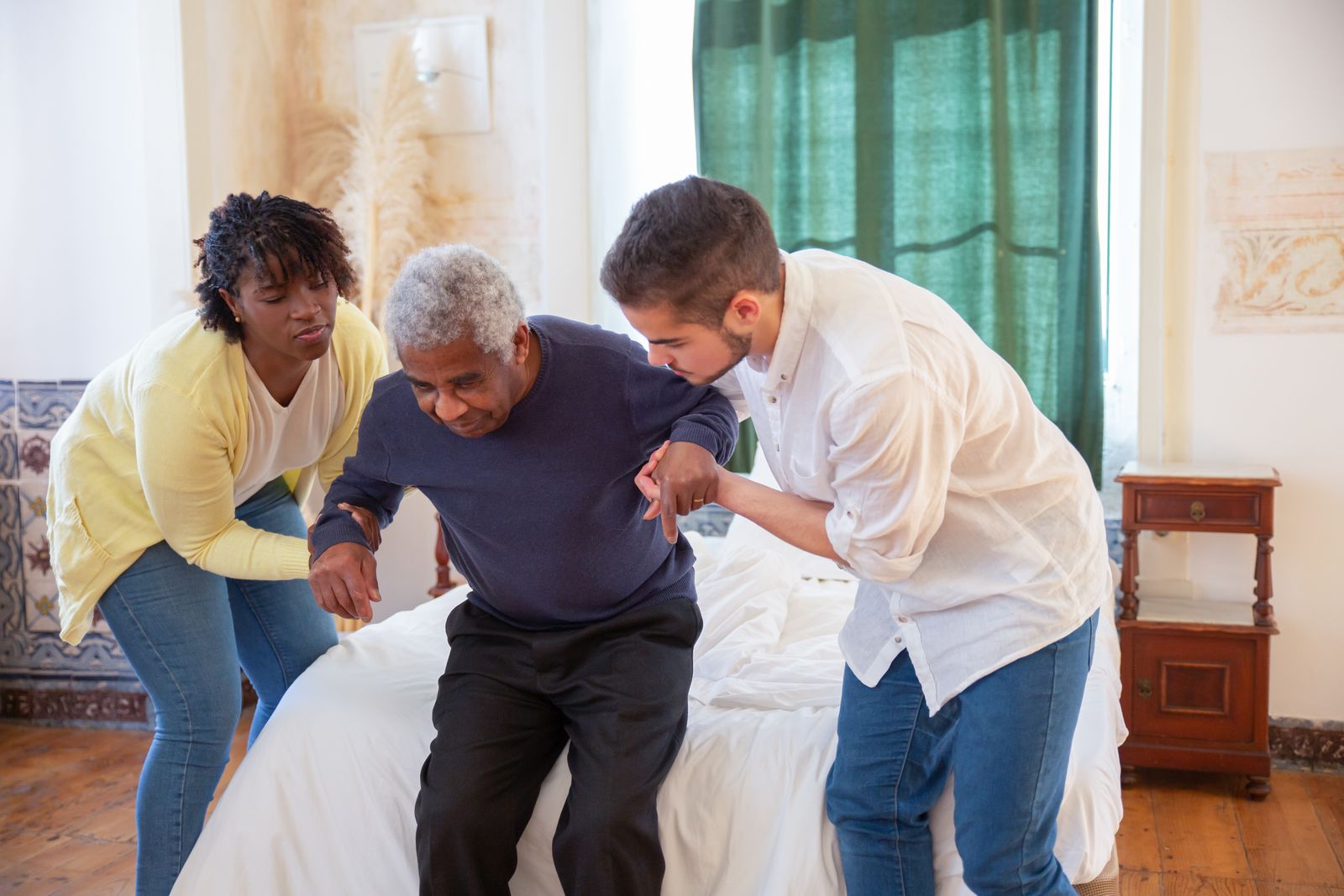Two caregivers helping an older man stand safely at home